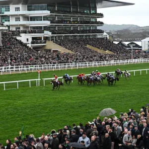 Exciting moment of a horse racing event at Cheltenham Races, showcasing the energy of the race and the vibrant crowd in the background.