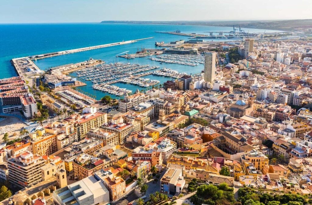 Scenic view of Alicante coastline with sandy beaches, historic castle, and vibrant cityscape under a sunny sky.