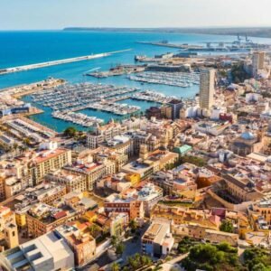 Scenic view of Alicante coastline with sandy beaches, historic castle, and vibrant cityscape under a sunny sky.