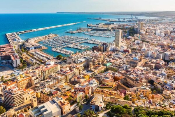 Scenic view of Alicante coastline with sandy beaches, historic castle, and vibrant cityscape under a sunny sky.