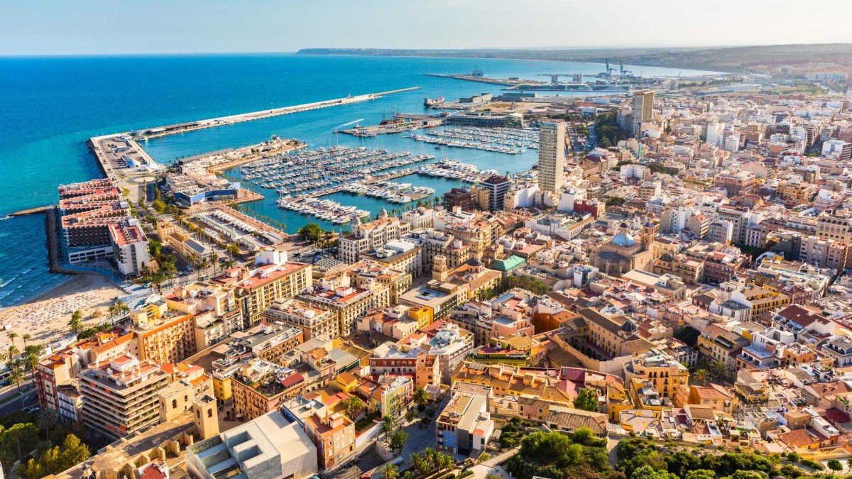 Scenic view of Alicante coastline with sandy beaches, historic castle, and vibrant cityscape under a sunny sky.